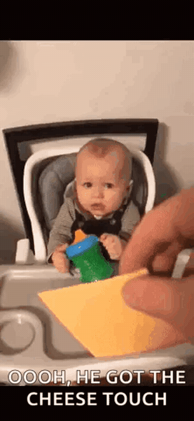 A Baby Is Sitting In A High Chair While A Person Takes A Piece Of Cheese From Him . GIF
