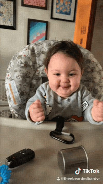 A Baby Is Sitting In A High Chair With A Sticker On His Shirt That Says Anna GIF