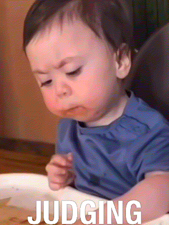 A Baby Is Sitting In A High Chair With The Word Judging Written On His Arm GIF