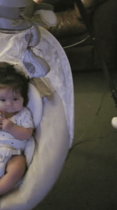 A Baby Is Sitting In A Swing With A White Cover On It GIF