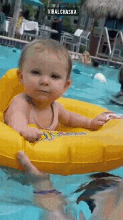 A Baby Is Sitting In An Inflatable Ring In A Swimming Pool . GIF