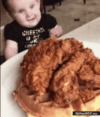 A Baby Is Sitting In Front Of A Plate Of Fried Chicken And A Waffle . GIF