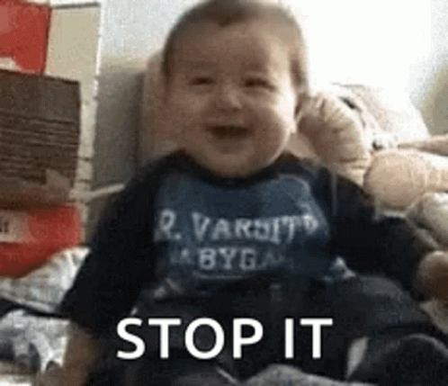 A Baby Is Sitting On A Bed And Smiling While Wearing A Shirt That Says Stop It . GIF