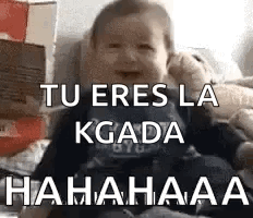 A Baby Is Sitting On A Bed With The Words `` Tu Eres La Kgada Hahahaa '' Written On The Screen . GIF