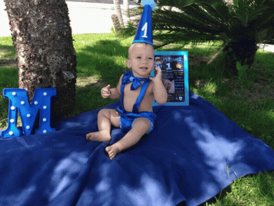 A Baby Is Sitting On A Blue Blanket With A Sign That Says " Miguel " On It GIF