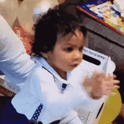 A Baby Is Sitting On A Chair With His Arms Outstretched And A Knife In His Hand . GIF