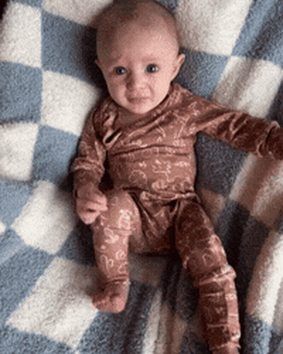 A Baby Is Sitting On A Checkered Blanket GIF