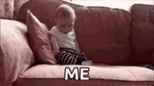 A Baby Is Sitting On A Couch Holding A Book And Says `` Me '' . GIF