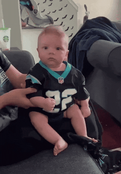 A Baby Is Sitting On A Couch Wearing A Number 25 Jersey GIF