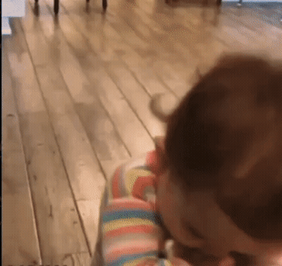 A Baby Is Sitting On A Wooden Floor With A Rainbow Striped Shirt On . GIF