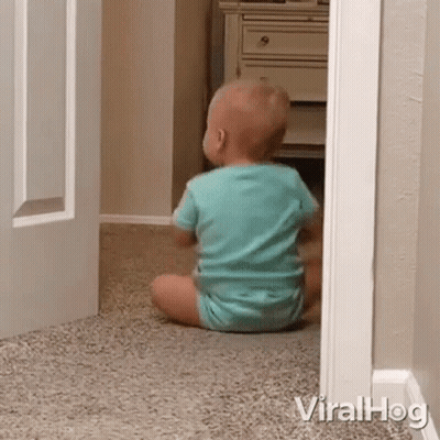 A Baby Is Sitting On The Floor In A Room Looking Out Of A Doorway . GIF