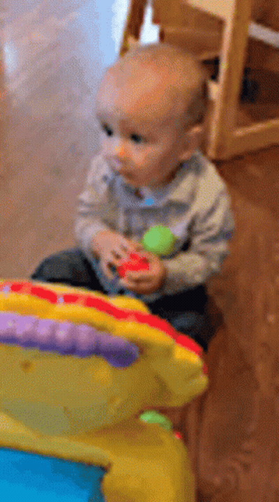 A Baby Is Sitting On The Floor Playing With A Toy GIF