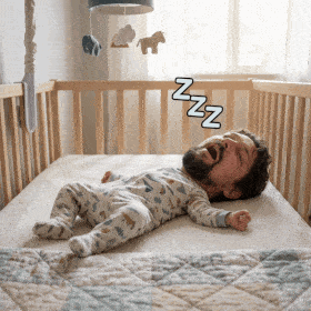 a baby is sleeping in a crib with a man 's head visible
