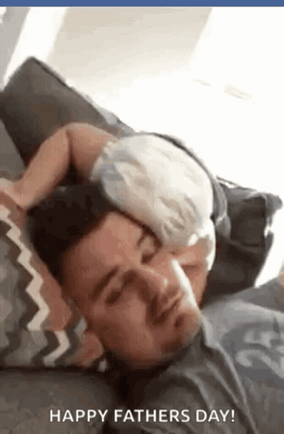 A Baby Is Sleeping On A Man 'S Head On A Couch . GIF