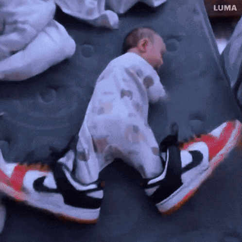 A Baby Is Sleeping On A Mattress Next To A Pair Of Nike Sneakers GIF