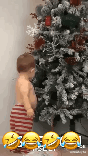 A Baby Is Standing In Front Of A Christmas Tree With Tears Running Down His Face . GIF