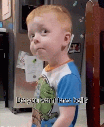 a baby is standing in front of a refrigerator with the words do you want taco bell written on it .