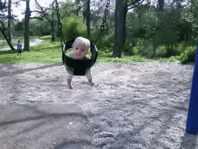 A Baby Is Swinging On A Swing Set In The Dirt GIF