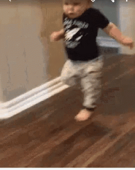 A Baby Is Walking On A Wooden Floor With A Piece Of Toilet Paper . GIF