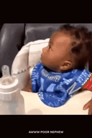 A Baby Is Wearing A Bib And Sitting In A High Chair . GIF