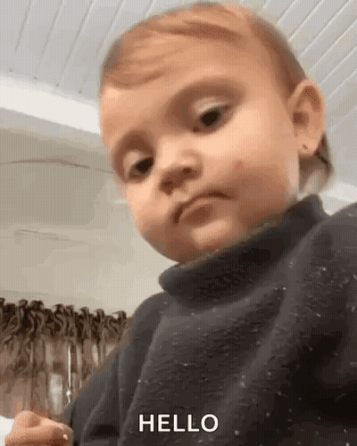 A Baby Is Wearing A Black Sweater And Making A Funny Face . GIF