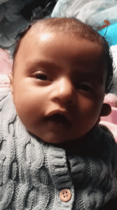 A Baby Is Wearing A Grey Sweater With A Button On It GIF