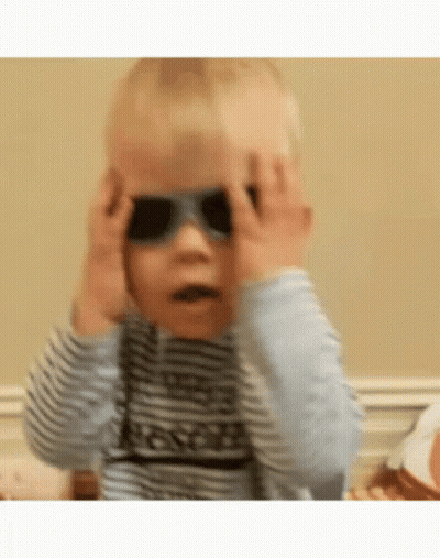 A Baby Is Wearing Sunglasses And Covering His Eyes . GIF