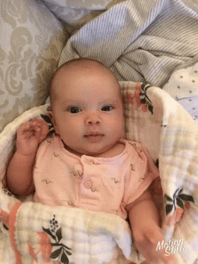 A Baby Is Wrapped In A Blanket And Looking At The Camera While Laying On A Bed . GIF