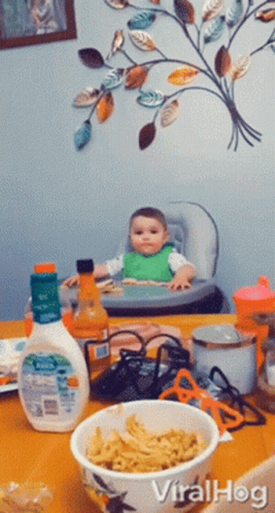 A Baby Sits In A High Chair Next To A Bowl Of Noodles GIF