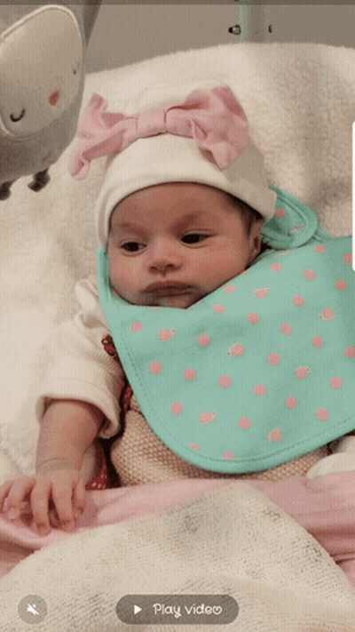 A Baby Wearing A Bib And A White Hat With A Play Video Button Below It GIF