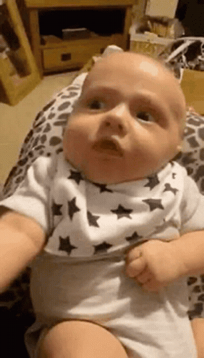 A Baby Wearing A Bib Is Being Held By A Person And Making A Funny Face . GIF