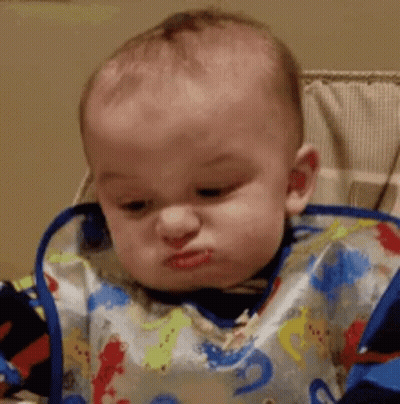 A Baby Wearing A Bib Is Sitting In A High Chair And Making A Funny Face . GIF