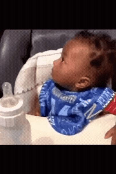 A Baby Wearing A Bib That Says Water On It Is Sitting In A High Chair GIF