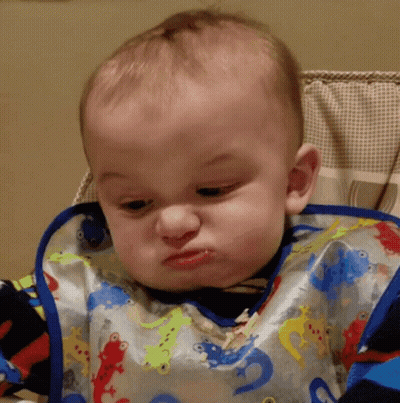 A Baby Wearing A Bib With Lizards On It Making A Funny Face GIF