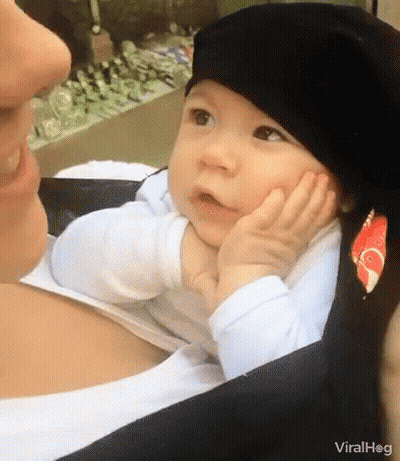 A Baby Wearing A Black Hat Is Sitting On A Woman 'S Lap . GIF