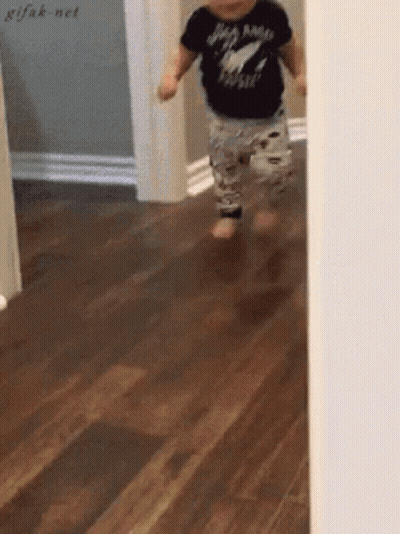 A Baby Wearing A Black Shirt That Says Rock N Roll Is Running On A Wood Floor GIF