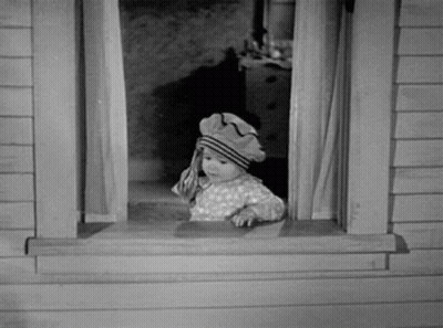 A Baby Wearing A Hat Looks Out A Window GIF