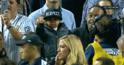 A Baby Wearing A Hat That Says Respect Stands In A Crowd GIF