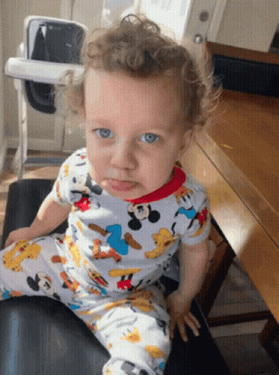 A Baby Wearing A Mickey Mouse Pajama Is Sitting On A Chair GIF