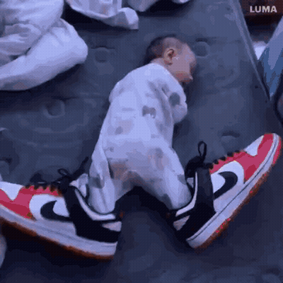 A Baby Wearing A Pair Of Nike Shoes Is Sleeping On A Bed . GIF