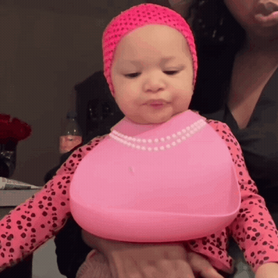 A Baby Wearing A Pink Bib And A Pink Headband Is Being Held By A Woman GIF