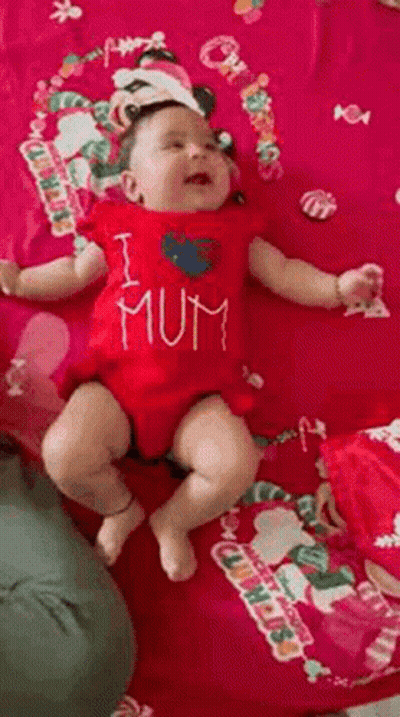 A Baby Wearing A Red Shirt That Says `` I Love Mum '' Is Laying On A Pink Blanket . GIF