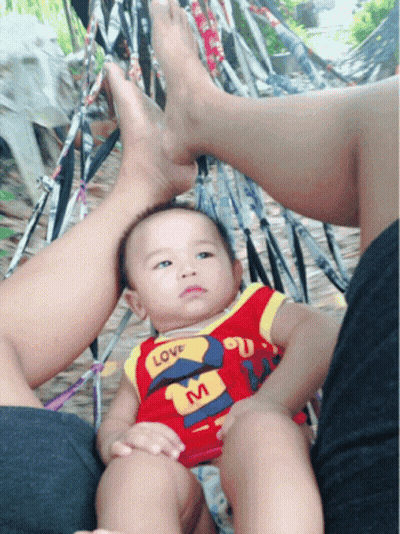 A Baby Wearing A Shirt That Says Love On It Sits In A Hammock GIF