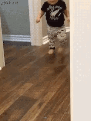 A Baby Wearing A Shirt That Says Rock N Roll Is Walking On A Wooden Floor GIF