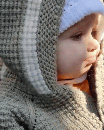 A Baby Wearing A Sweater With A Hood And A White Hat GIF