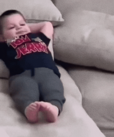 A Baby Wearing A Tom Jerry Shirt Laying On A Couch GIF