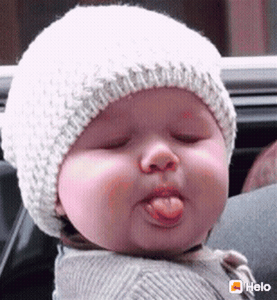 A Baby Wearing A White Hat Is Sticking Its Tongue Out . GIF