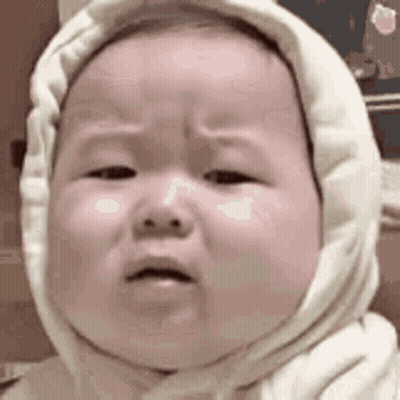 a baby wearing a white hooded sweater is crying .