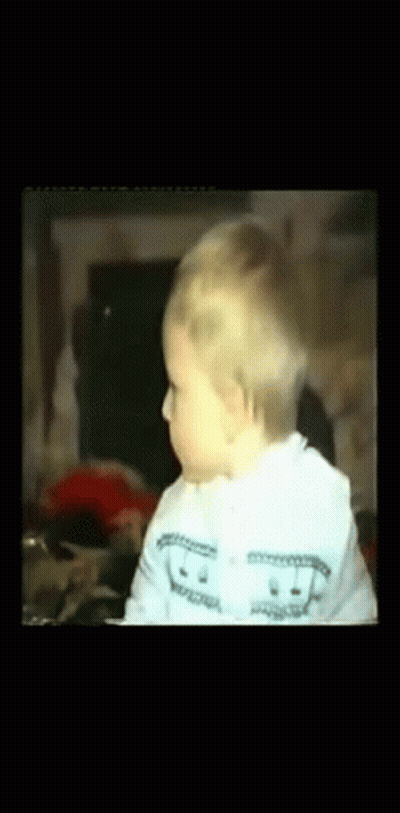 A Baby Wearing A White Sweater With A Smiley Face On It GIF