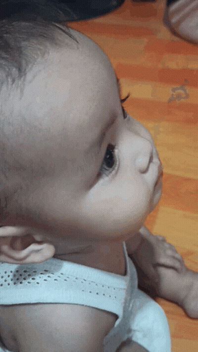 A Baby Wearing A White Tank Top Looks Up At Something GIF